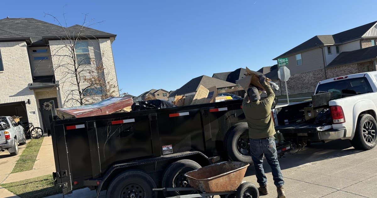 A Royse City Junk Removal crew member loading debris into the dump trailer on a residential street